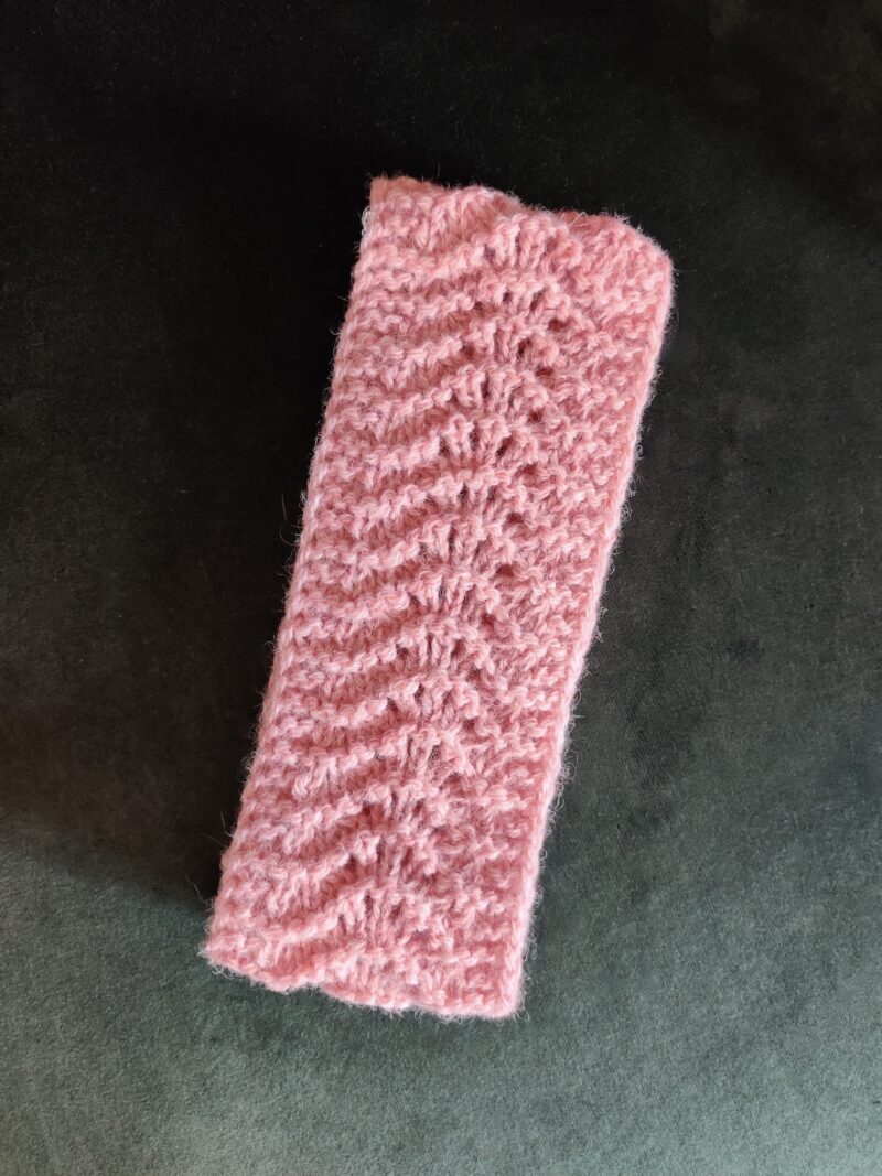 bandeau rose en laine shetland posé sur un fond vert foncé