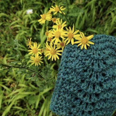bandeau vert en laine posé dans l'herbe à côté de fleurs sauvages